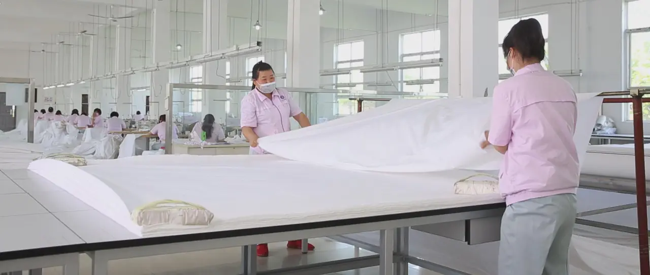 Workers checking white hospitality fabric on an inspection table